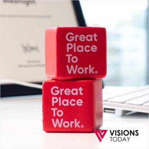 Two red blocks stacked on a desk, each reading 'Great Place To Work' with Visions Today logo in the corner.