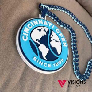 Circular blue pendant with a world map design and the text 'Cincinnati Open Since 1899,' on a blue chain. Visions Today watermark in the corner.